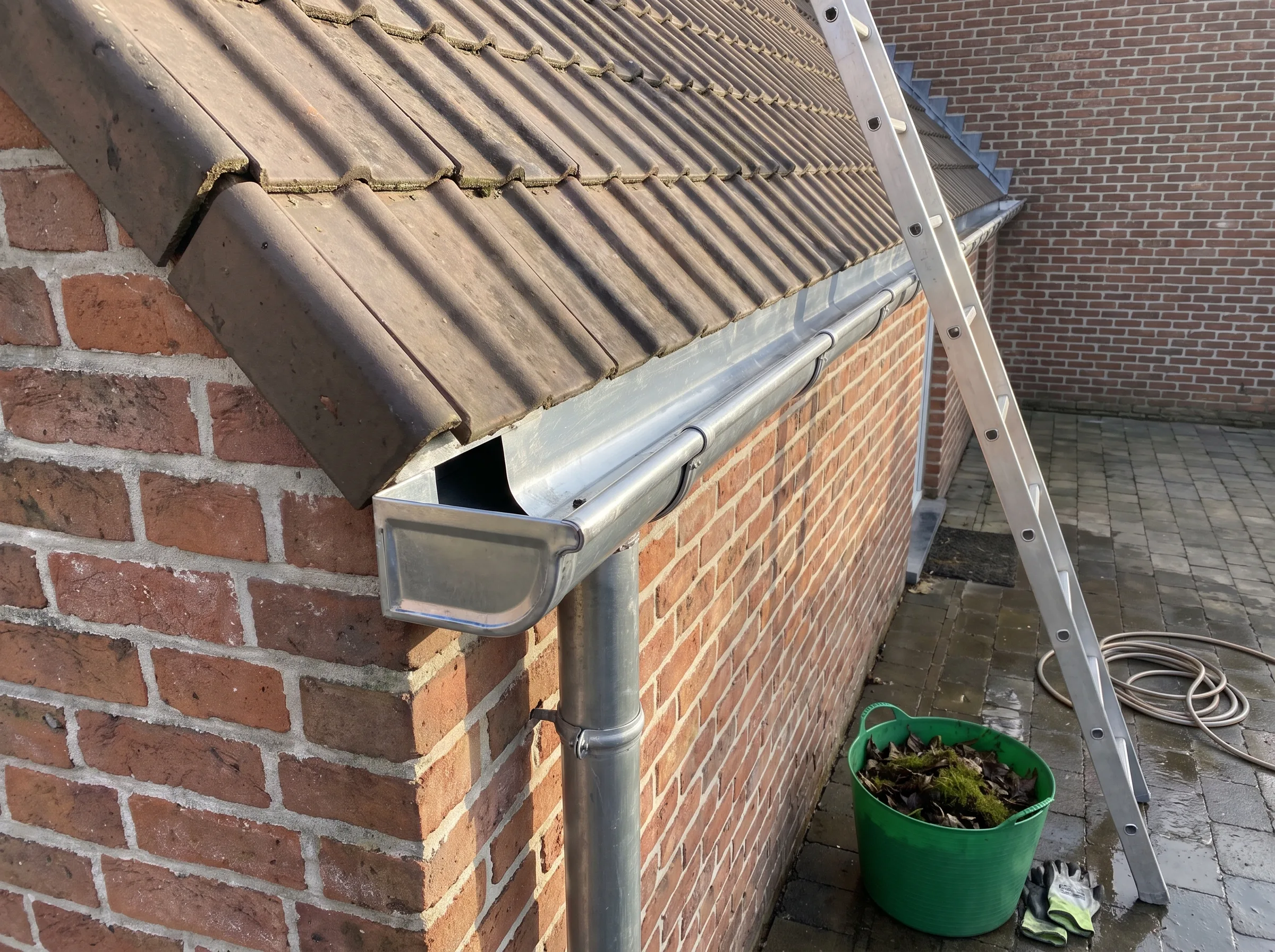 Dakgoot en hellend dak met ladder en groene emmer voor reiniging